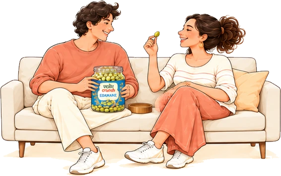 Two people on a sofa passing a jar of roasted edamame between them